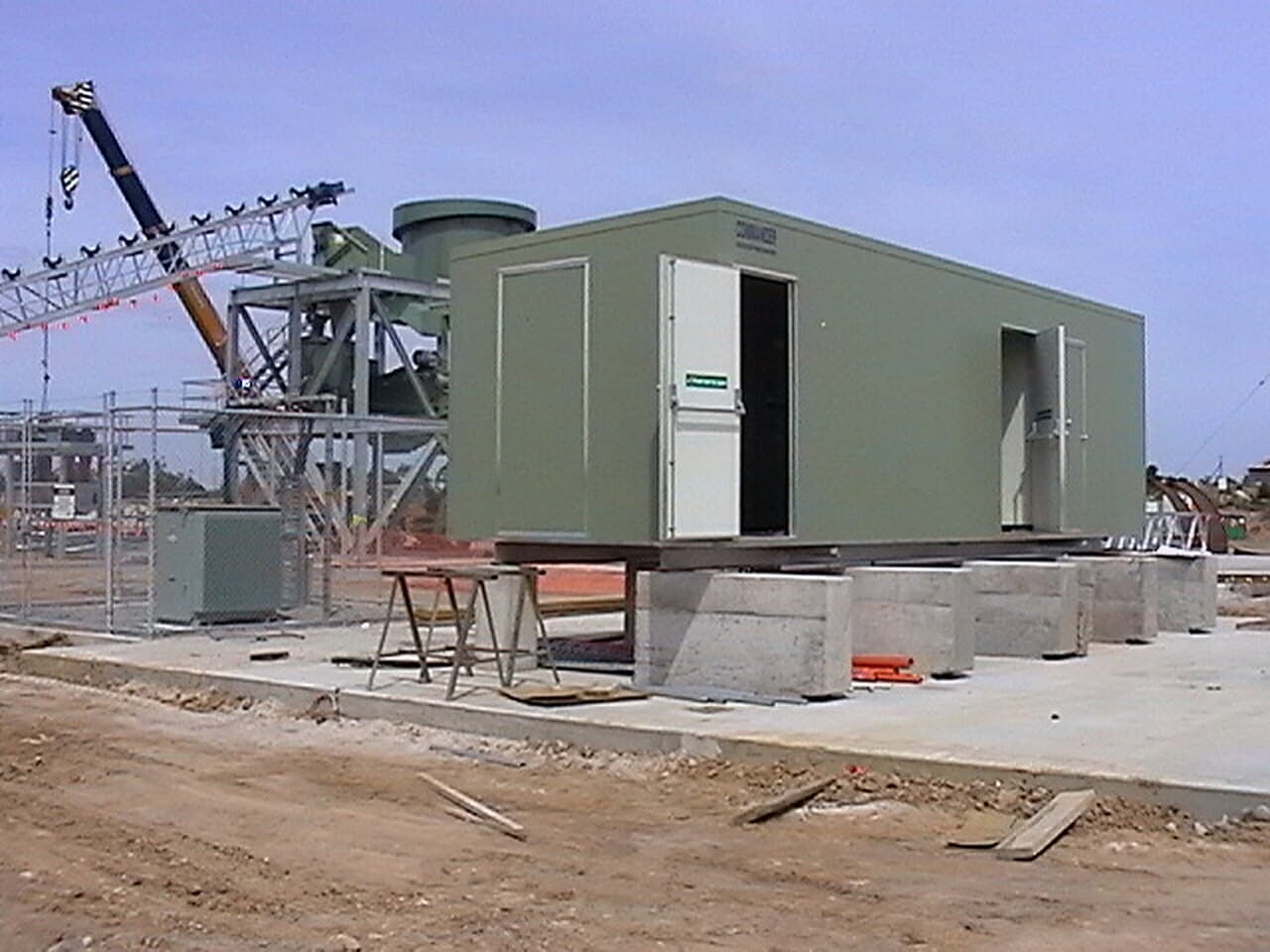 Prefabricated switchroom being positioned by crane on concrete plinths at a processing plant